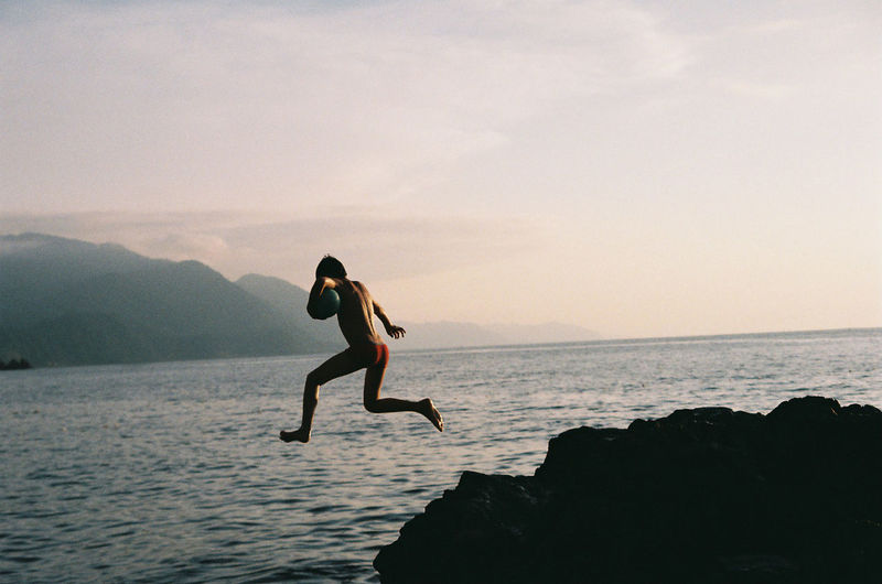 Rear view of shirtless boy jumping in sea