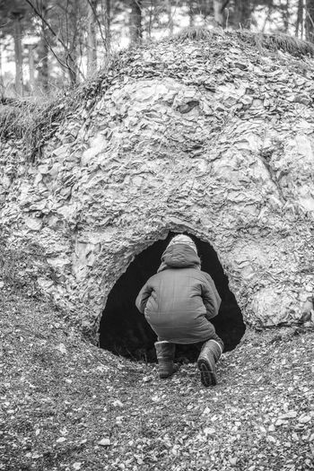 Rear view of person peeking in ruined bunker at forest