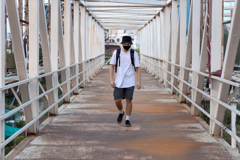 Young millennial walking on footbridge while wearing a protective mask to prevent covid-19 infection