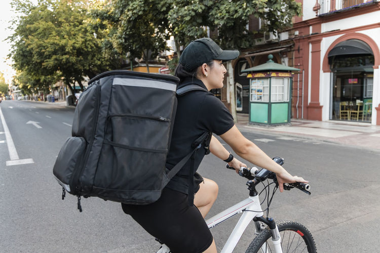 Female delivery person with backpack riding cycle on road