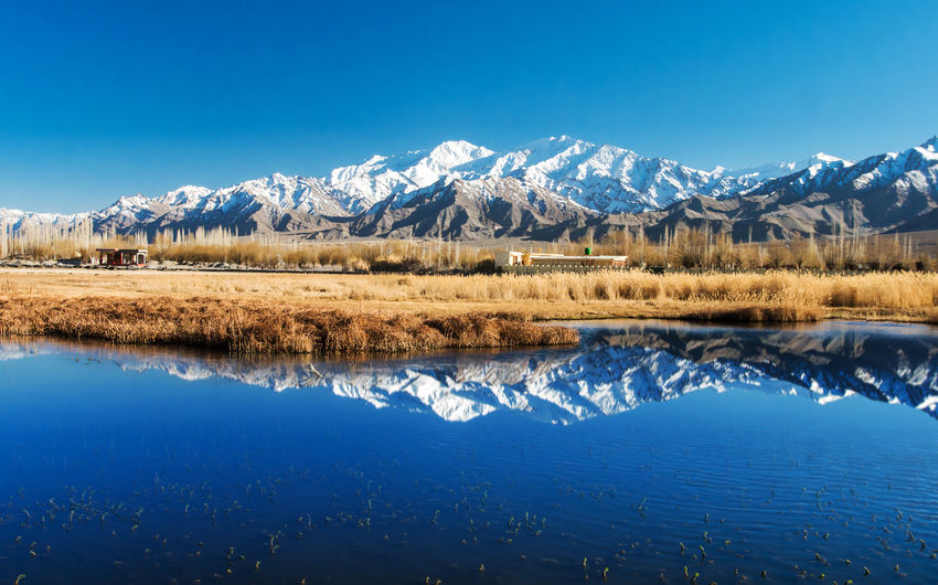 Scenic view of lake by snowcapped mountains against blue sky