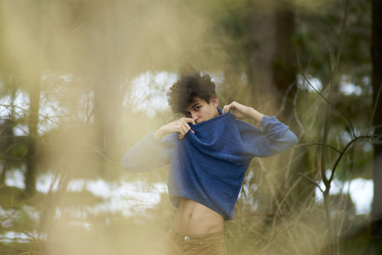 Young man wearing sweater while standing at forest