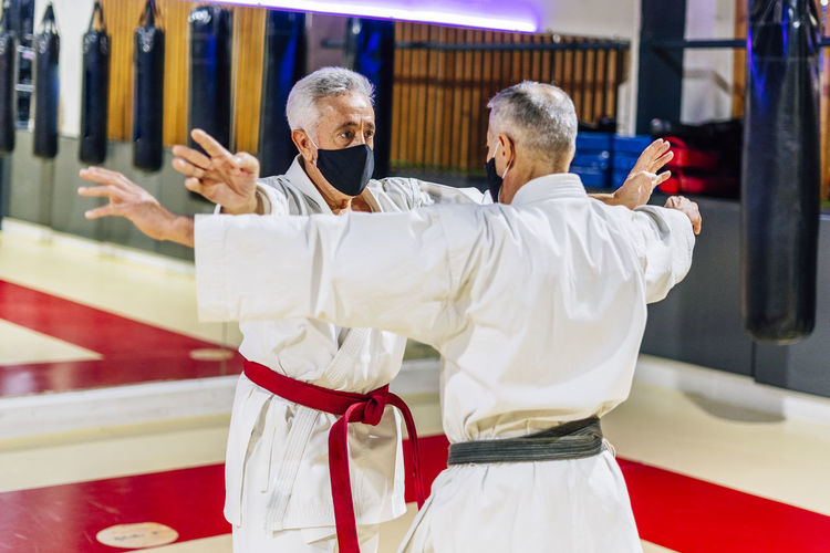 Men with arms outstretched wearing face masks while practicing karate in health club