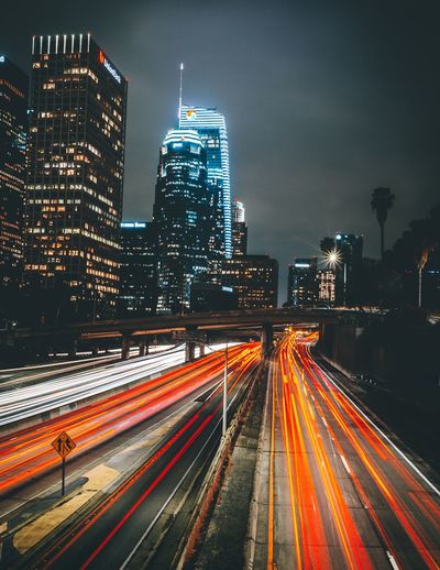 Light trails on road by illuminated buildings in city at night