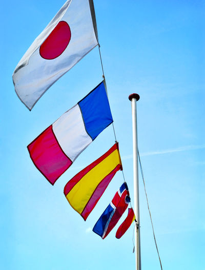 Low angle view of various flags waving on rope against blue sky