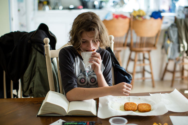 Teen girl takes a bite of a hash brown while she reads her book