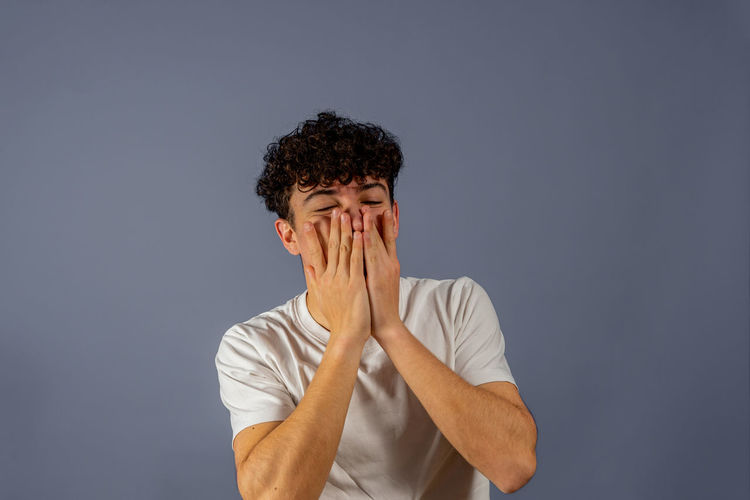 Portrait of young man covering face against gray background
