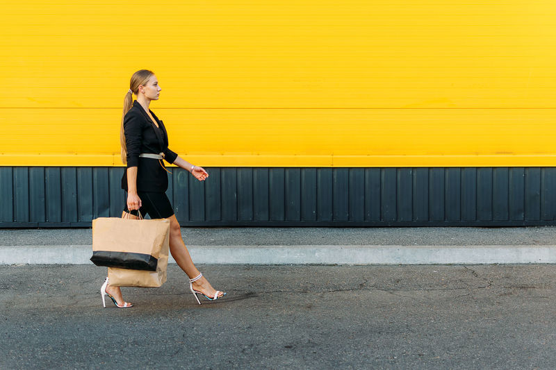 Shopping, sale concept. stylish fashionable young woman walking and holding shopping bags on yellow