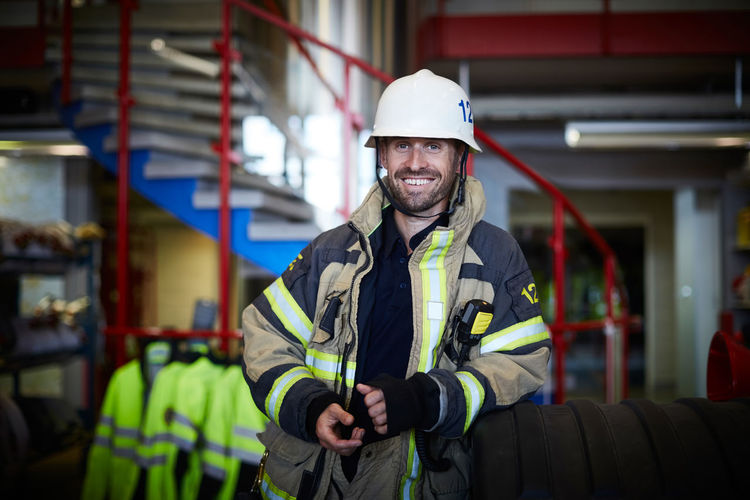 Portrait of smiling firefighter wearing protective suit at fire station