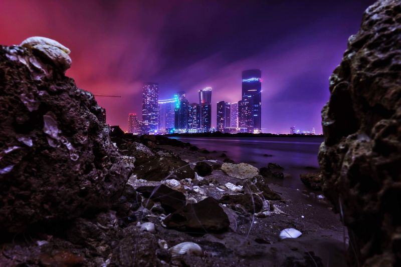 Illuminated buildings by rocks against sky in city at night