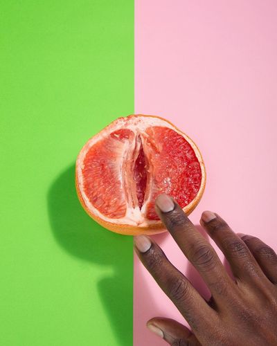 Cropped hands of person touching grapefruit over two tone background