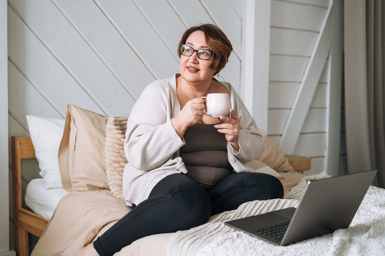 Young woman using mobile phone while sitting on bed at home