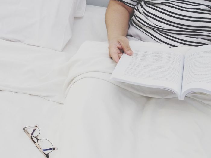 Midsection of woman reading book on bed