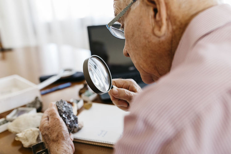 Retired senior male looking through magnifying glass at mineral