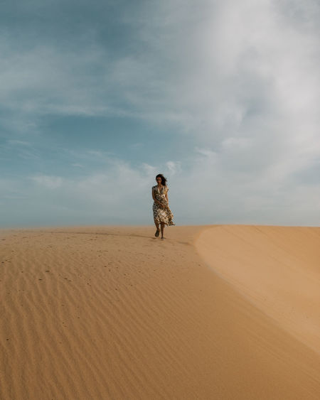 Woman standing on a sand dune in desert against sky