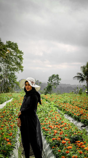 Full length portrait of woman standing by flowering plants against sky