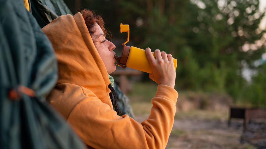Side view of woman drinking water by tent