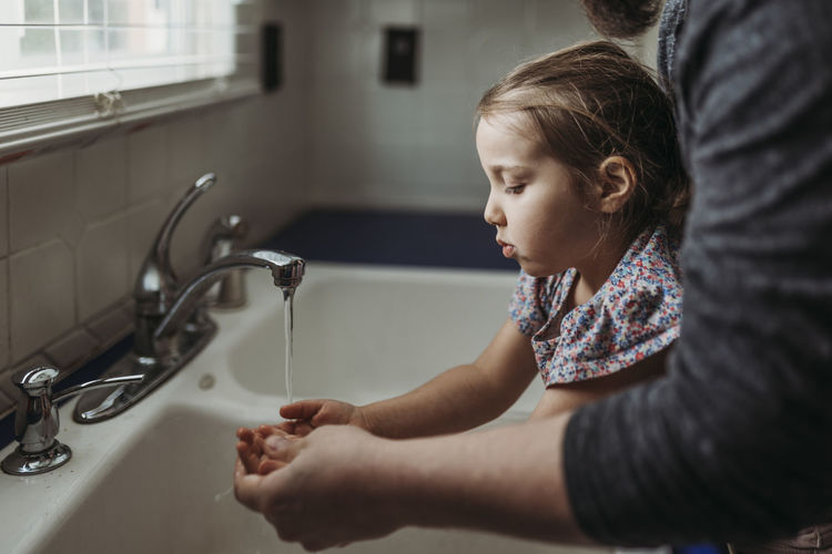 Side view of young girl having hands washed by dad
