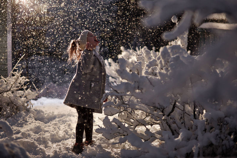 Girl in snow catches snowflakes under a lantern