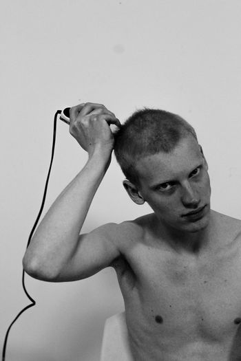 Portrait of shirtless man trimming hair against wall