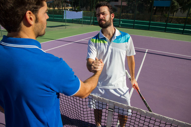 Male friends shaking hands while standing on tennis court