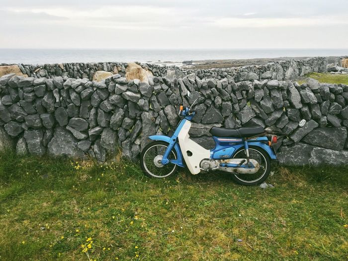 Moped leaning on stone wall against sky