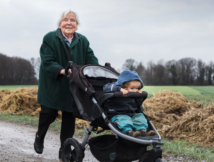 Full length of grandmother pushing baby stroller with granddaughter