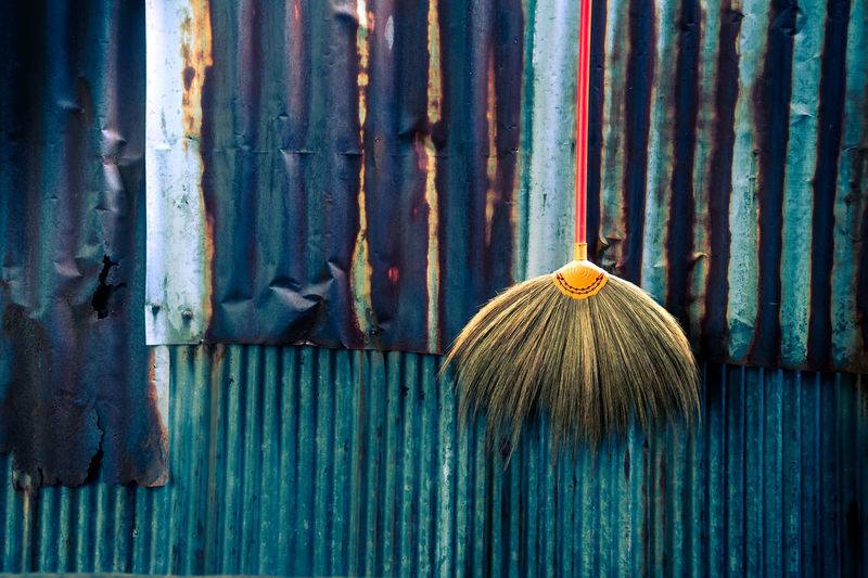 Broom hanging by rusty metal fence