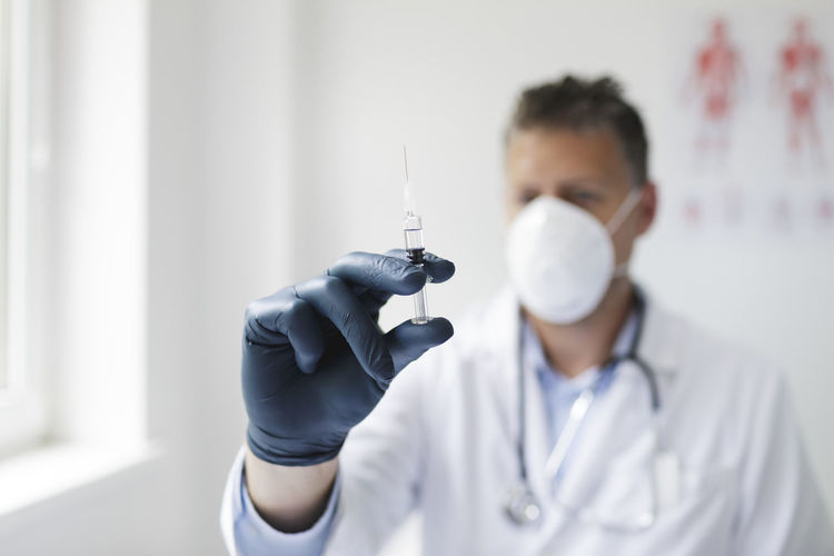 Close-up of doctor wearing mask holding syringe at hospital