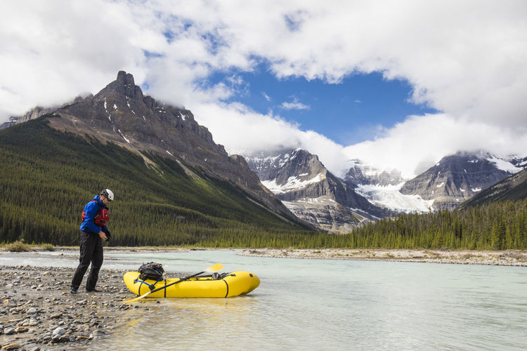 Man exploring the rocky mountains in a packraft stops for a break.