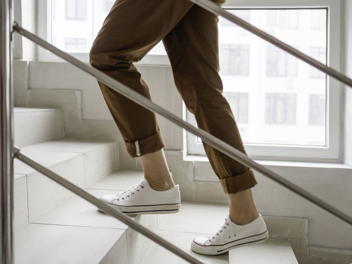 Woman in white sneakers and khaki trousers goes upstairs. white staircase in apartment building. 