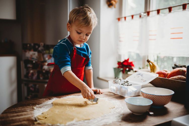 Young child making christmas cookies in the kitchen at home with apron