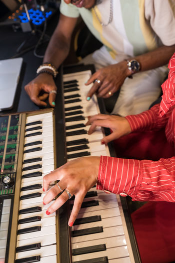 Cropped unrecognizable female musician playing electric piano and black male singer listening to melody in headphones while recording music in studio