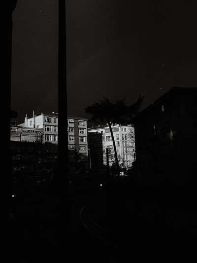 Silhouette buildings by street against sky at night
