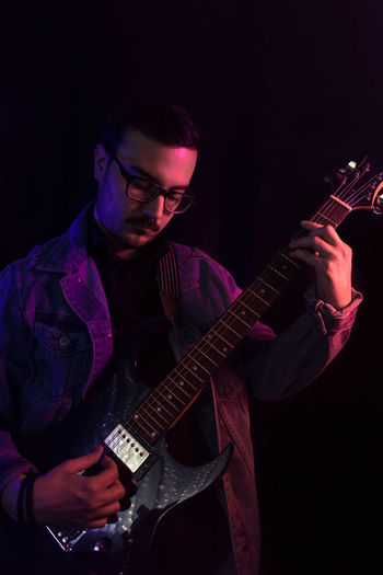 Young adult plays electric guitar under colored lights