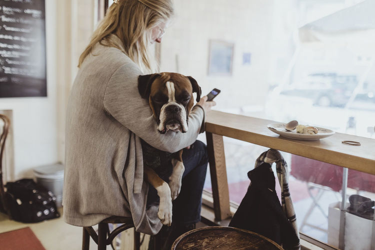 Side view of young woman using smart phone while sitting with dog at cafe