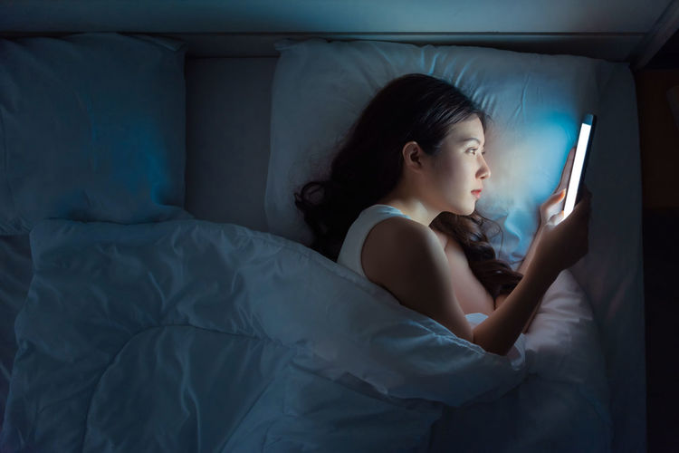 Young woman using mobile phone while sitting in bed