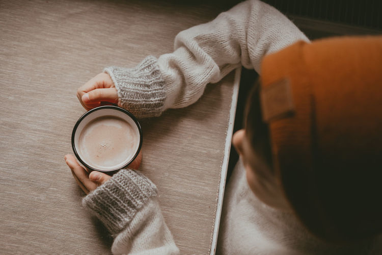 Hands in a sweater hold hot cocoa, in a red mug, top view. a cozy photo with a mug in hand 