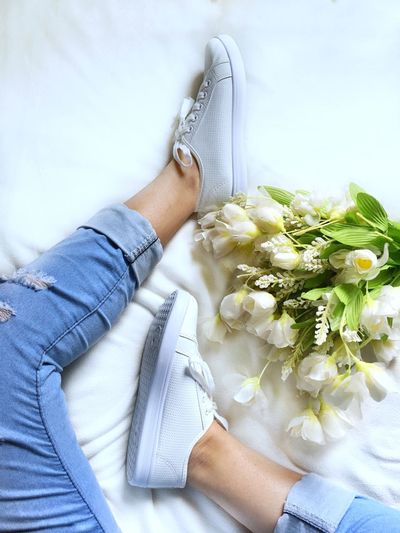 Low section of woman sitting on bed with white flowers