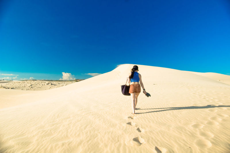 Young woman walking in desert against clear blue sky