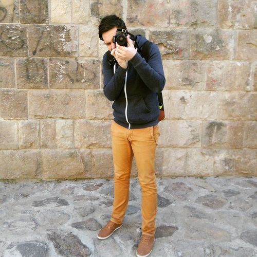 Man photographing while standing against stone wall
