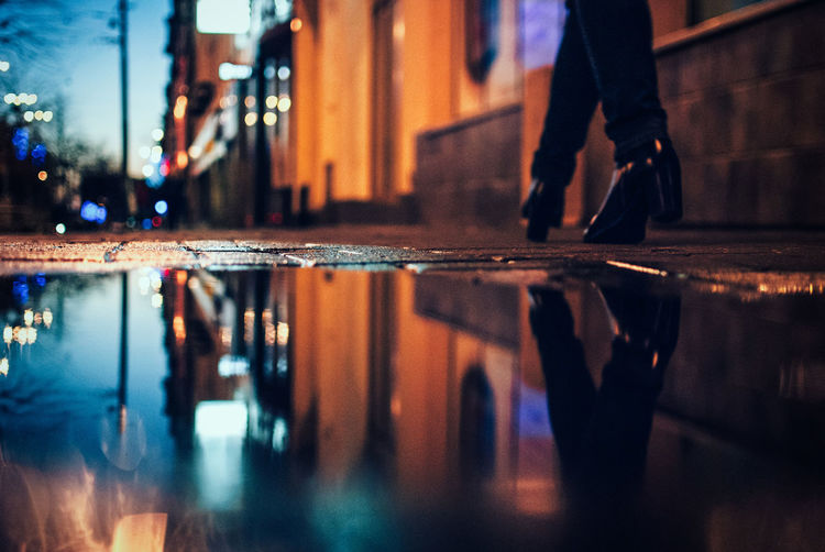 Low section of woman walking by puddle at sidewalk