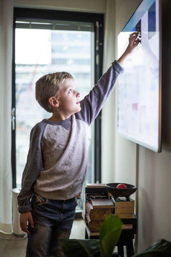 Boy touching digital display of smart television set at modern home