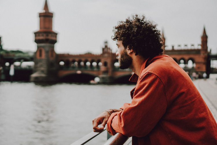 Man standing on bridge over river in city against sky