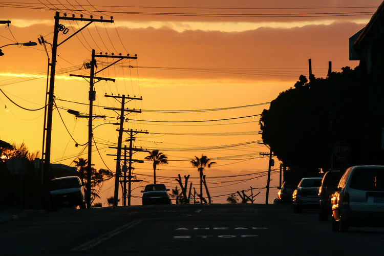 Electricity pylons on road at sunset