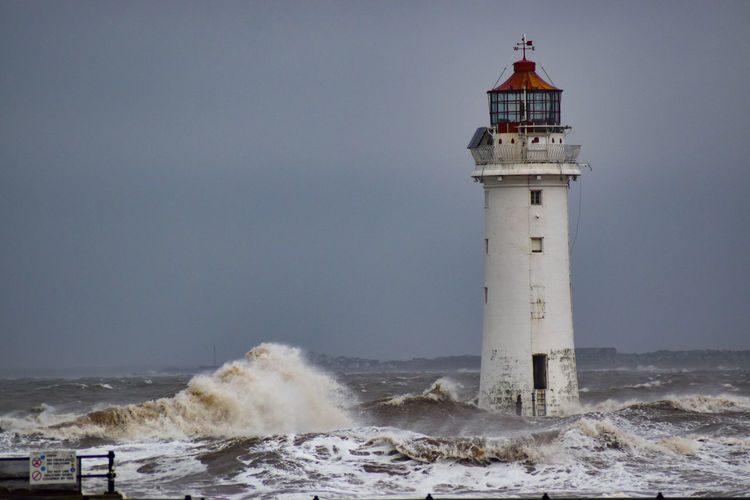 Lighthouse on beach by sea against sky