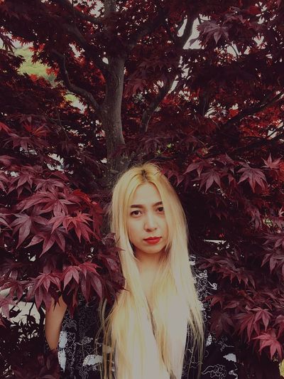 Portrait of blond woman standing amidst maroon leaves