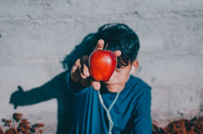 Teenage boy holding apple while listening music on headphones