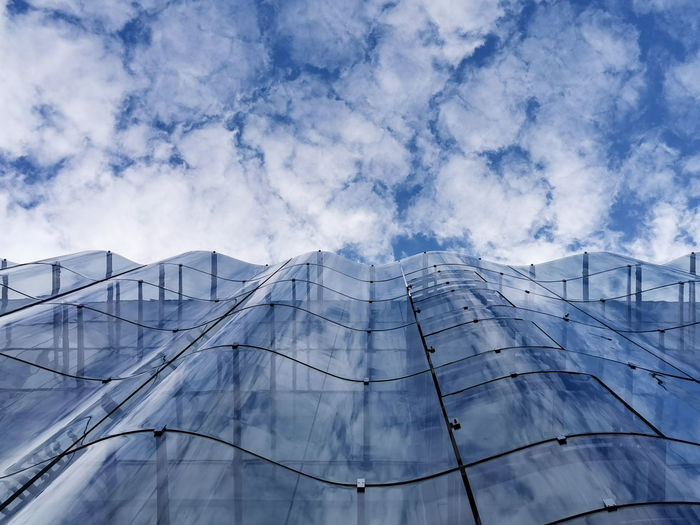 Wavy glass curtain wall facade of a nice modern building, sky and clouds reflecting on it