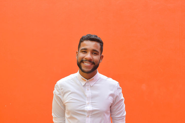 Portrait of smiling young man standing against red wall